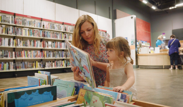 A photo of a woman and child reading a story book at a library. 