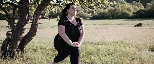 A woman stretches outdoor with a field and trees behind