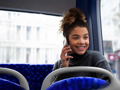Photo of a person smiling whilst talking on the phone on the bus.