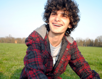 young adult male sat outside on grass with sky behind